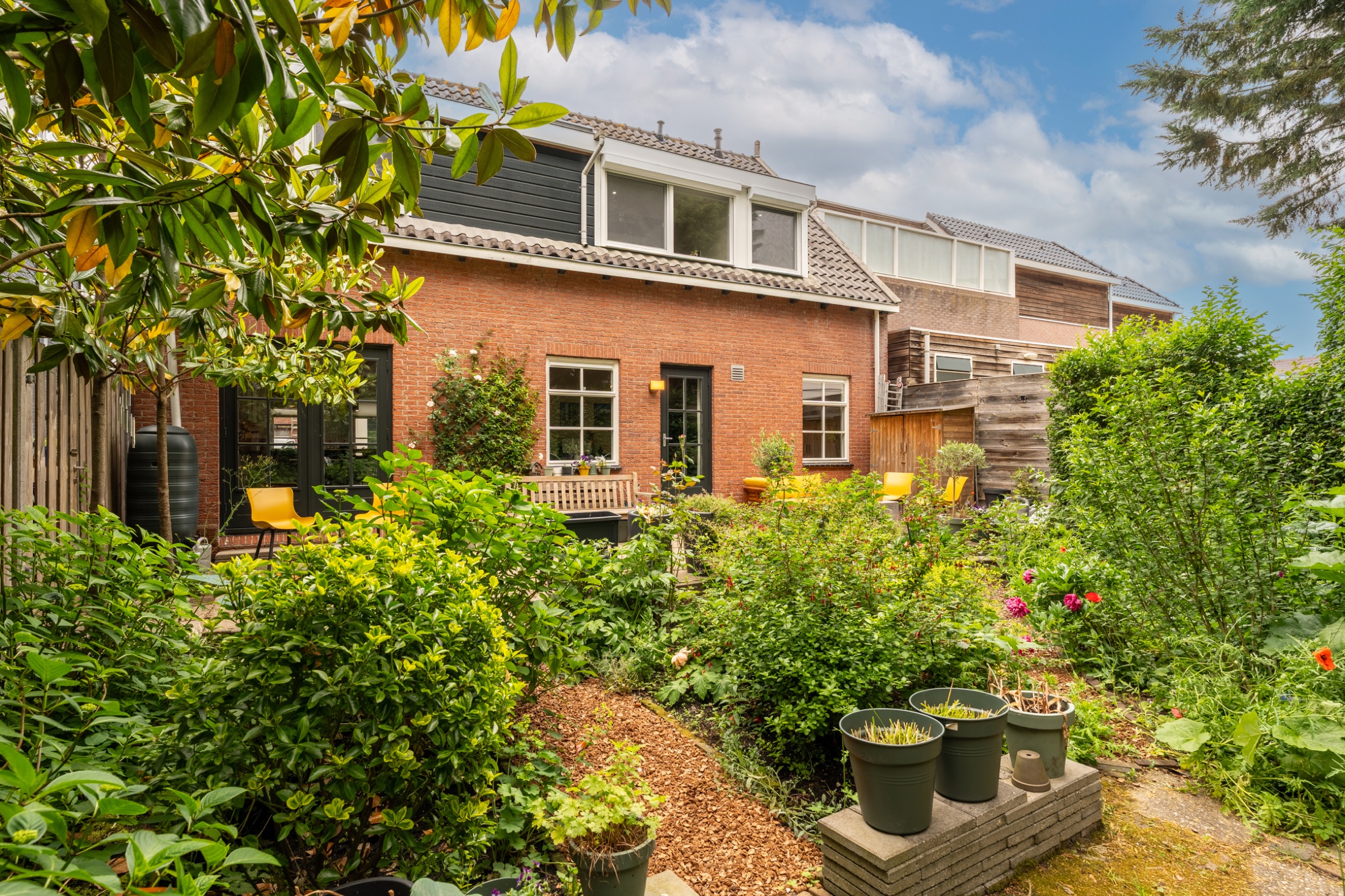 Achtertuin van Dorpsstraat 67, met terras, beplanting en het huis op de achtergrond